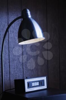 Royalty Free Photo of a Dim Desk Lamp and Retro Clock Against Wood Paneling at Night