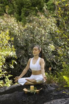 Royalty Free Photo of a Woman Sitting on a Boulder in the Forest Meditating With a Candle in Maui, Hawaii