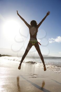 Back view of girl in bikini jumping enthusiastically on beach in Maui, Hawaii, USA.