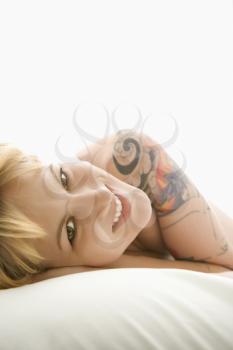 Nude Caucasian young adult woman lying on bed smiling at viewer.