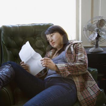 Royalty Free Photo of a Woman Sitting in a Green Chair Reading a Paper