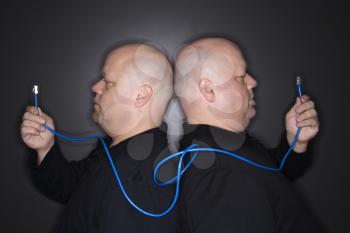 Caucasian bald mid adult identical twin men standing back to back holding ethernet cable.