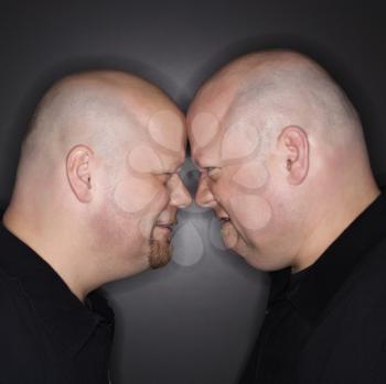 Royalty Free Photo of Identical Twin Men Standing Face to Face With Angry Expressions