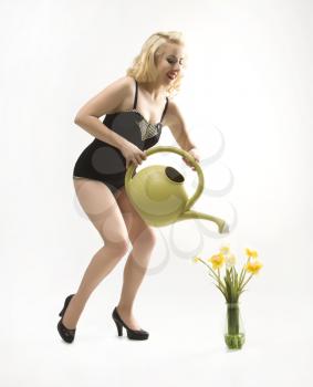 Attractive Caucasian woman wearing retro swimsuit in pinup pose watering flowers.