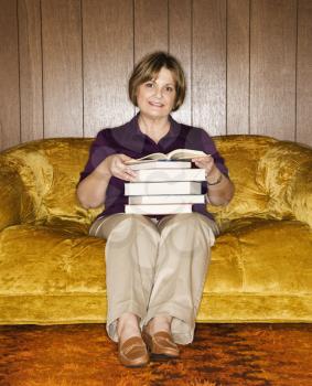 Royalty Free Photo of a Caucasian Woman Sitting on a Couch in a Living Room Holding a Stack of Books