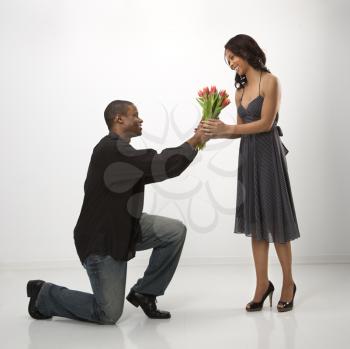 Royalty Free Photo of a Man on His Knees Giving a Woman a Bouquet of Flowers