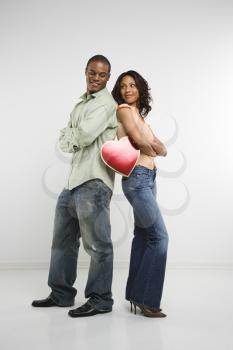 Royalty Free Photo of a Couple Standing Back to Back With Arms Crossed Smiling and Holding a Valentine Heart