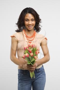 Studio shot of multiethnic mid-adult stylish woman holding bouquet of tulips smiling and looking at viewer. 