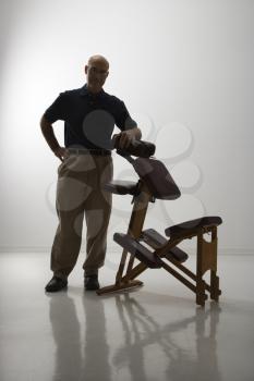 Royalty Free Photo of a Silhouette Middle-Aged Male Massage Therapist Standing With His Elbow on a Massage Chair