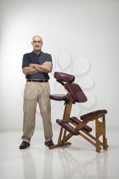 Royalty Free Photo of a Middle-Aged Male Massage Therapist Standing Beside a Massage Chair