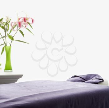 Royalty Free Photo of a Spa Scene of a Massage Table With Purple Sheets and a Table With Pink Easter Lilies in a Green Vase