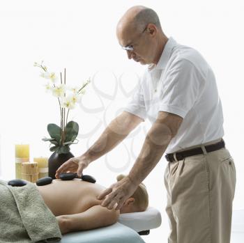 Royalty Free Photo of a Male Massage Therapist Placing Hot Stones on a Woman' Back