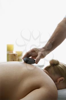 Royalty Free Photo of a Male Massage Therapist Placing Hot Stone on the Back of a Middle-Aged Woman Lying on a Massage Table