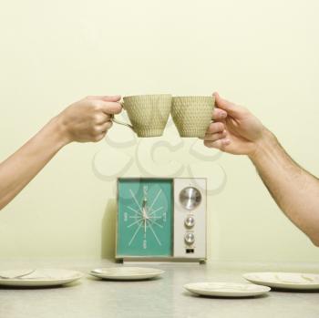 Royalty Free Photo of Male and Female Hands Toasting with Coffee Cups Across a Retro Kitchen Table Setting