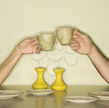 Royalty Free Photo of Male and Female Hands Toasting With Coffee Cups Across a Retro Kitchen Table Setting