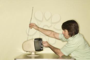 Royalty Free Photo of a Man Sitting at a 50's Retro Dinette Set Tapping an Old Television Set