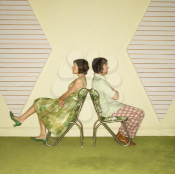 Royalty Free Photo of a Couple Wearing Vintage Clothing Sitting Back to Back in Green Vinyl Chairs with Arms Crossed