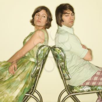 Royalty Free Photo of a Couple Wearing Vintage Clothing Sitting Back to Back in Green Vinyl Chairs With Arms Crossed Looking Angry