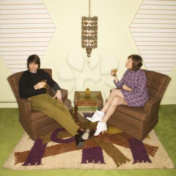 Royalty Free Photo of a Couple Seated in Retro Chairs Smiling and Drinking