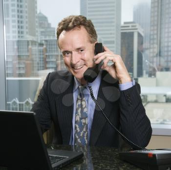 Royalty Free Photo of a Businessman on the Phone in Office with Skyline in the Background