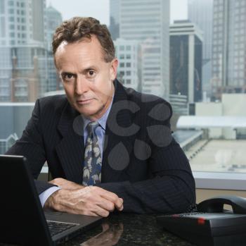 Middle-aged Caucasian male in office with skyline in background.