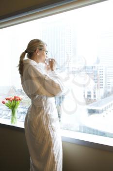 Mid-adult Caucasian woman with coffee cup looking out window.