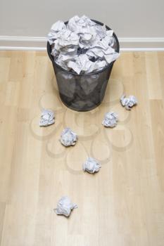 Royalty Free Photo of a Wire Mesh Trash Can With Crumpled Paper Scattered Around