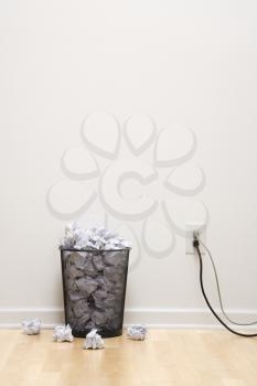 Royalty Free Photo of a Full Wire Mesh Trash Can With Crumpled Paper Next to an Electrical Outlet and Plugs