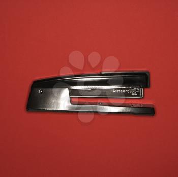 Royalty Free Photo of a Black Stapler on a Red Background