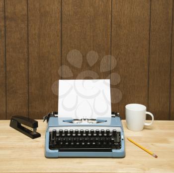Royalty Free Photo of a Vintage Typewriter, Coffee Cup, Pencil and Stapler on a Desk