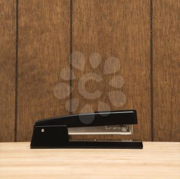 Royalty Free Photo of a Black Stapler on a Desk With Wooden Paneling