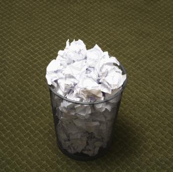 Royalty Free Photo of a Wire Mesh Trash Can Filled with Crumpled Paper on a Green Carpet