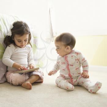 Royalty Free Photo of Little Girls Sitting on a Bedroom Floor Looking at a Book