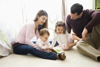 Royalty Free Photo of a Family Sitting on a Bedroom Floor Reading a Book