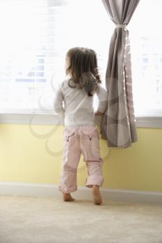 Royalty Free Photo of a Toddler Girl Standing on Her Tip Toes Looking Out the Window