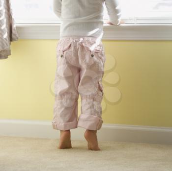 Royalty Free Photo of a Toddler Girl Standing on Tip Toes Looking Out of the Window