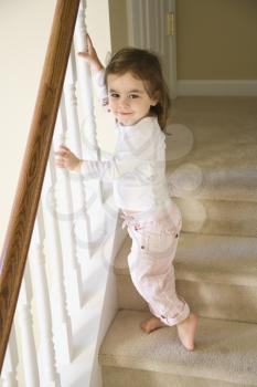 Caucasian girl toddler standing on carpeted stairs holding onto railing.