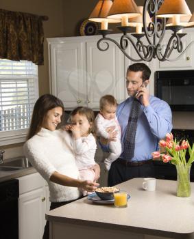 Royalty Free Photo of a Mother and Father in a Kitchen Busy With Children and Cellphone