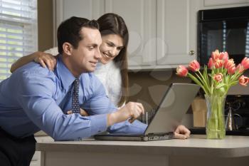 Royalty Free Photo of a Couple in a Kitchen Looking at a Laptop Computer
