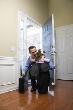 Royalty Free Photo of a Businessman at an Open Door Holding a Briefcase and Hugging His Daughter