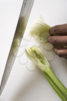African-American male hands using large kitchen knife to chop fennel.