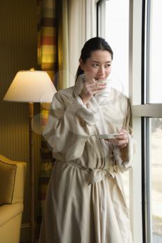 Royalty Free Photo of a Woman in a Bathrobe Drinking Coffee and Looking Out the Window