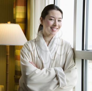 Taiwanese mid adult woman in bathrobe smiling at viewer with arms crossed.