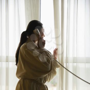 Royalty Free Photo of a Woman in a Bathrobe Talking on the Phone and Looking Out the Window
