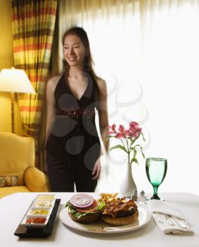 Royalty Free Photo of Room Service Cheeseburger Meal With Flowers and Woman in the Background