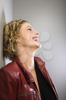 Royalty Free Photo of a Woman in a Red Jacket Leaning Back Against a Wall Laughing