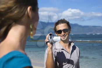 Royalty Free Photo of a Man on a Beach Pointing a Video Camera at a Woman