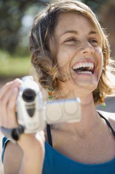 Royalty Free Photo of a Woman Outdoors Holding a Video Camera Laughing
