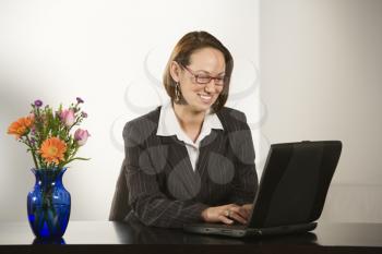 Royalty Free Photo of a Businesswoman Sitting at a Desk Smiling While Typing on a Laptop