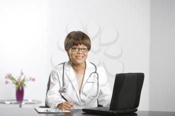Royalty Free Photo of a Female Doctor Sitting at a Desk Working on Her Laptop